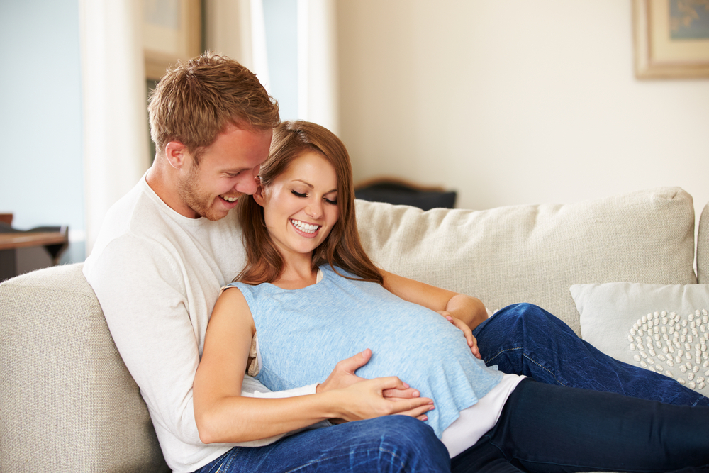 Couple,With,Pregnant,Woman,Relaxing,On,Sofa,Together